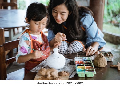 mother and daughter painting ceramic pot in pottery workshop