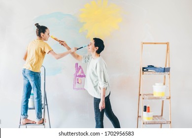 Mother   daughter painting house wall   having fun  Woman playing and daughter   drawing nose each other  Repair In Apartment 