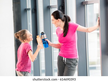 Mother And Daughter In Pink Shirts With Sport Bottles In Gym