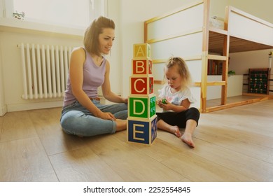 mother and daughter play with wooden cubes, with letters on the faces and able to hold smaller ones; the room is bright and clear - Shutterstock ID 2252554845