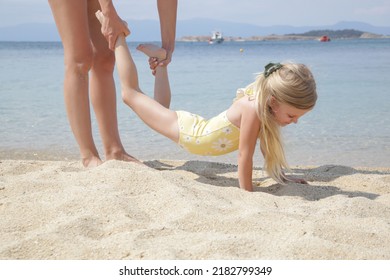 Mother and daughter playing on beach, exercising for a wheelbarrow race.