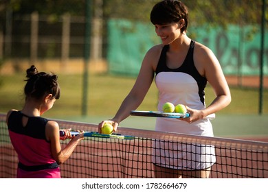 a mother and daughter playing tennis together outdoors on a clay court - Powered by Shutterstock