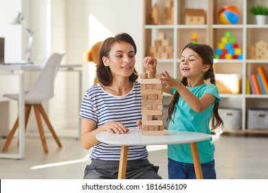 Mother and daughter playing wood block tower stacking game in cozy modern nursery at home. Ethnic babysitter engaging little girl in quiet activities developing concentration and hand eye coordination