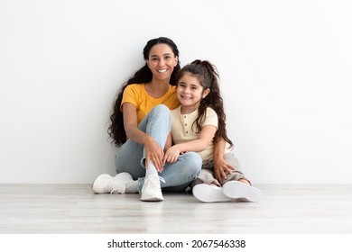 Mother And Daughter. Portrait Of Happy Loving Family Of Two Mom And Female Child Bonding Together While Sitting On Floor Near White Wall At Home, Young Woman And Her Kid Embracing And Smiling