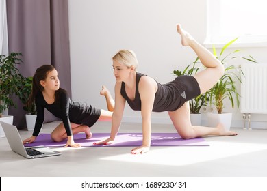 Mother And Daughter Practicing Online Yoga Lesson At Home At Quarantine Isolation Period During Coronavirus Pandemic. Family Doing Sport Together Online From Home. Healthy Lifestyle