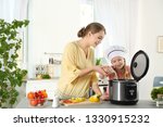 Mother and daughter preparing food with modern multi cooker in kitchen