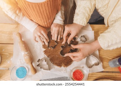 Mother and daughter preparing gingerbread cookies using star and gingerbread man shaped cookie cutters on a wooden table - Powered by Shutterstock