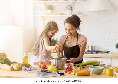 Mother and daughter preparing tasty food at kitchen. Mommy teaching lovely kid to cook. Happy smiling mom and loving child spending time together at home. Healthy meal and dinner preparation
