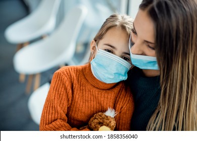 Mother And Daughter With Protective Face Masks Sitting In A Waiting Room At Medical Clinic. Focus Is On Little Girl. 