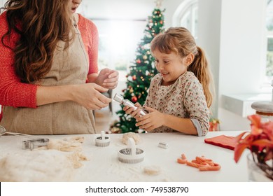 Mother And Daughter Pulling A Christmas Cracker. Woman Making Christmas Cookies Using Dough Moulds And Cutters.