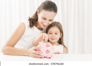 Mother And Daughter Putting Coins Into Piggy Bank. Family Budget And Savings Concept. Junior Savings Account Concept