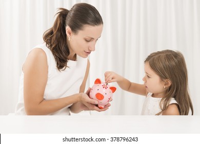 Mother And Daughter Putting Coins Into Piggy Bank. Family Budget And Savings Concept. Junior Savings Account Concept