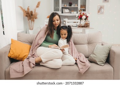 Mother and daughter are reading a book on the sofa in the living room. home schooling concept. - Shutterstock ID 2071332887