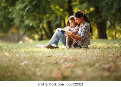 Mother and daughter relaxing in park.She reading a fairytale to her daughter - Powered by Shutterstock