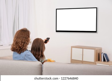 Mother and daughter with remote control sitting on couch and watching TV at home, space for design on screen. Leisure and entertainment - Shutterstock ID 1227646840