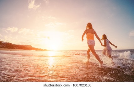 Mother And Daughter Running Inside The Water On Tropical Beach - Mum Playing With Her Kid In Holiday Vacation Next To The Ocean - Family Lifestyle And Love Concept - Focus On Bodies Silhouette