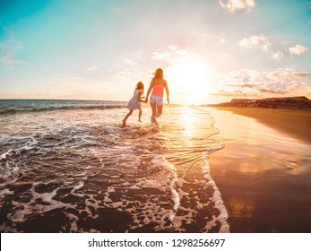 Mother And Daughter Running Inside The Water On Tropical Beach - Mum Playing With Her Kid In Holiday Vacation Next To The Ocean - Family Lifestyle And Love Concept - Focus On Bodies Silhouette