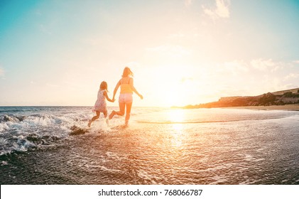 Mother And Daughter Running Inside The Water On Tropical Beach - Mum Playing With Her Kid In Holiday Vacation Next To The Ocean - Family Lifestyle And Love Concept - Focus On Silhouettes