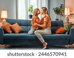 Mother and daughter in the same clothes are sitting on a blue sofa and looking at each other with their noses touching each other. Candid sincere authentic family moments.