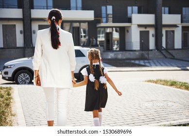 Mother With Daughter In School Uniform Outdoors Near White Car.