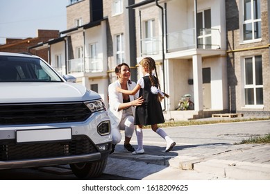 Mother With Daughter In School Uniform Outdoors Near White Car.