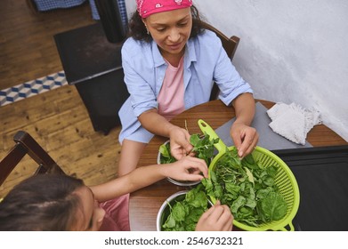 Mother and daughter share a bonding moment as they wash and prepare fresh greens in a cozy kitchen setting, promoting family connection and healthy eating. - Powered by Shutterstock