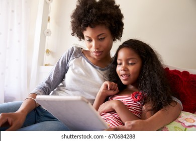 Mother And Daughter Siting On Bed Using Digital Tablet