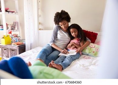 Mother And Daughter Siting On Bed Reading Book Together