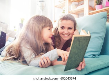 Mother and daughter sitting on sofa at home and reading book together
