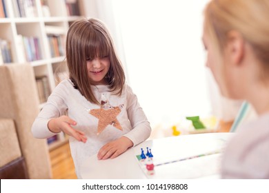 Mother And Daughter Sitting In A Playroom, Playing A Ludo Game; Daughter Rolling The Dice