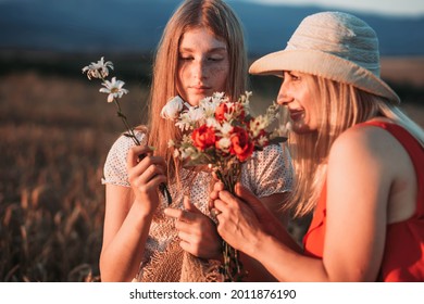 Mother And Daughter Smelling Flowers In The Field.