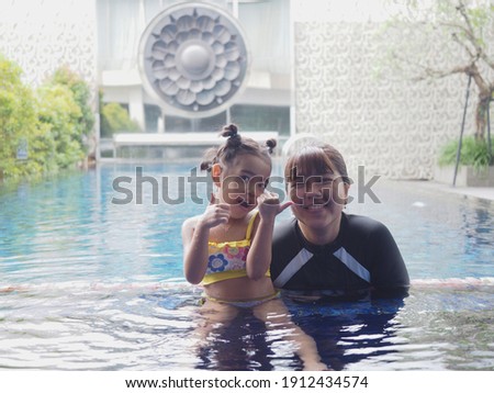 Mother and daughter smiling and happily playing in the swimming pool