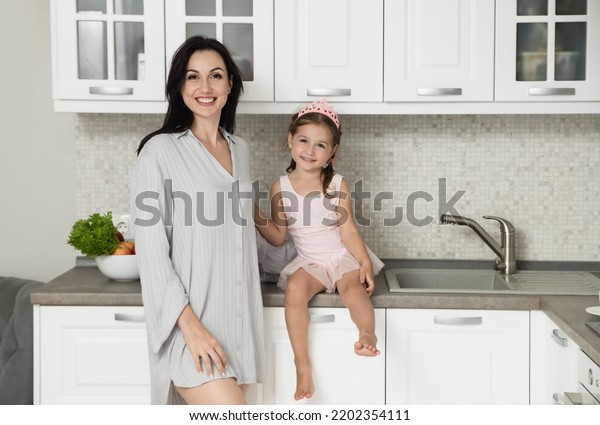 Mother and\
daughter is smiling and talking at the kitchen. Mom with her little\
princess at home. Woman and little girl in pink crown together.\
Facial expression. Selective\
focus.