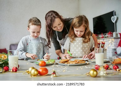 Mother, Daughter And Son Is Cooking Christmas Cookies. Family Is Preparing Holiday Food. Christmas Baking And Happy Holidays. Two Glasses Of Milk On The Table For Santa.