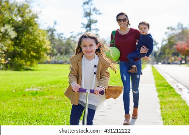 Mother Daughter And Son Family In The Park Walking With Ball And Skate Scooter