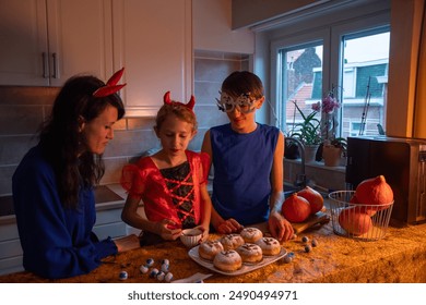 Mother, daughter and son in Halloween costumes draw skulls with cocoa powder and powdered sugar on sweet buns in a darkened room, baking together a traditional dessert for the holiday  - Powered by Shutterstock