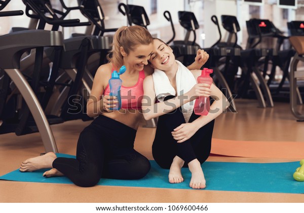 Mother And Daughter In Sportswear Sitting On Mat Drinking Water At The Gym They Look Happy 9001