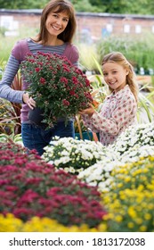 Mother And Daughter Standing Beside Colorful Flowers In Garden Centre.