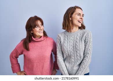 Mother And Daughter Standing Over Blue Background Looking Away To Side With Smile On Face, Natural Expression. Laughing Confident. 