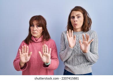 Mother And Daughter Standing Over Blue Background Moving Away Hands Palms Showing Refusal And Denial With Afraid And Disgusting Expression. Stop And Forbidden. 