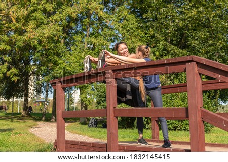 Mother and daughter stretching legs together on top of wooden staircase in public park on sunny summer morning. Family outdoor sports theme.