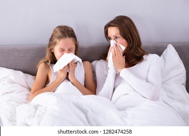 Mother And Daughter Suffering From Cold Blowing Her Nose With Handkerchief On Bed - Powered by Shutterstock