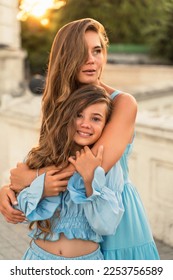 Mother daughter sunset. in blue dresses with flowing long hair against the backdrop of sunset. The woman hugs and presses the girl to her. - Shutterstock ID 2253756589