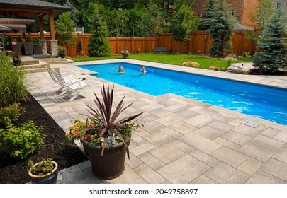 Mother And Daughter Swimming In New Back Yard Pool With Dog A Patio Of Pavers And Green Lawn And Gardens