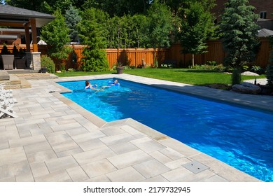 Mother And Daughter Swimming In New Back Yard Pool With  Patio Of Pavers And Green Lawn And Gardens