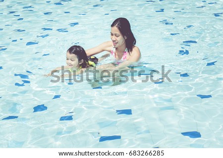Mother and daughter are swimming in the pool.