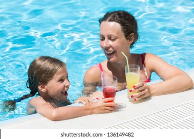Mother and daughter swimming in the pool with a drink in hand, focus on glass.