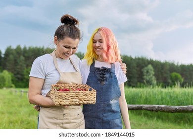 Mother and daughter teenager in aprons walking together with basket of fresh strawberries, nature, farm, beautiful landscape background. Healthy organic food, farm work and hobbies - Powered by Shutterstock