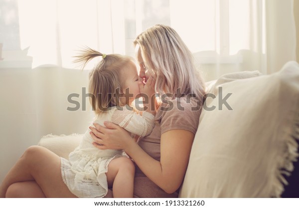 Mother and  daughter toddler playing, kissing,\
hugging  and smiling, enjoy at the sofa, spending time at home.\
Moments of tenderness . Happy loving family. Good time at home.\
Family single mother