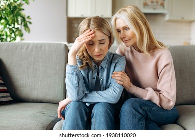 Mother and daughter together at living room. Loving mature mom sits on the couch and hugs her young adult daughter, stroking her, sympathizes, family relationship and values concept